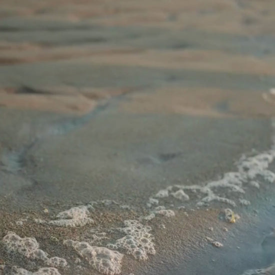 Video showcasing a person applying Skog body oil on her legs  then walking through the beach barefoot 