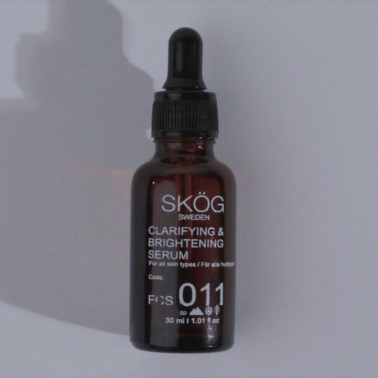 "Video showcasing SKÖG Clarifying & Brightening Serum .Dark amber bottle , black dropper cap with a white text on a lable , Person Drops a drop of serum onto her hand  gently rubbing on her hands then  applying gently  on all over her face . Contains Elderflower Oil, Sea Buckthorn Oil, Jojoba Oil, Grapeseed Oil, All natural ingredients 